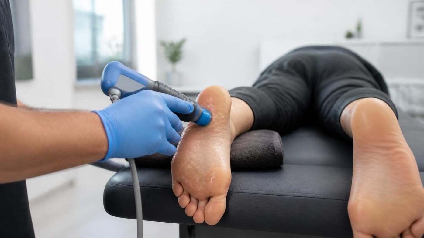 Clinician applying a handheld shockwave therapy device to the bottom of a patient's heel for plantar fasciitis
